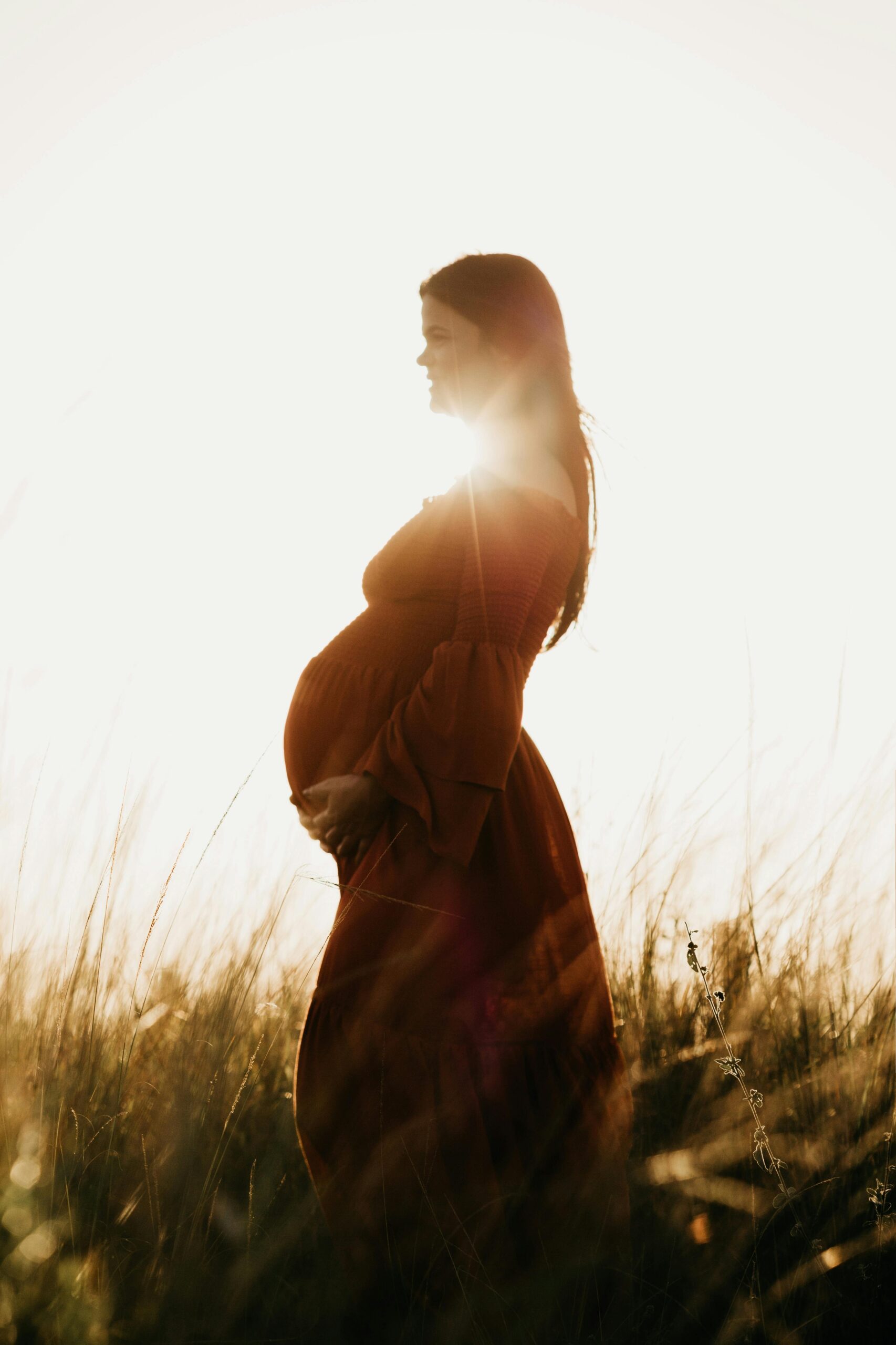 Serene pregnant woman in a sunlit field, embracing nature and motherhood.